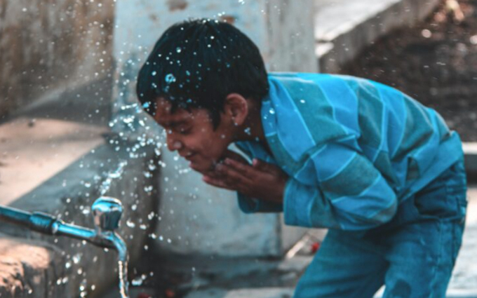 Niño en el patio de un colegio bebiendo agua.